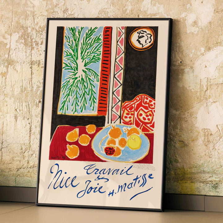 Henri Matisse Nice Travail et Joie poster with palm fronds, fruit on a blue plate, and bold red and black shapes, framed and displayed in modern living room decor