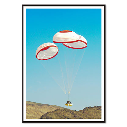 CST-100 crew capsule landing with three parachutes over desert landscape by NASA and The Boeing Company poster artwork, with black aluminium frame on white background