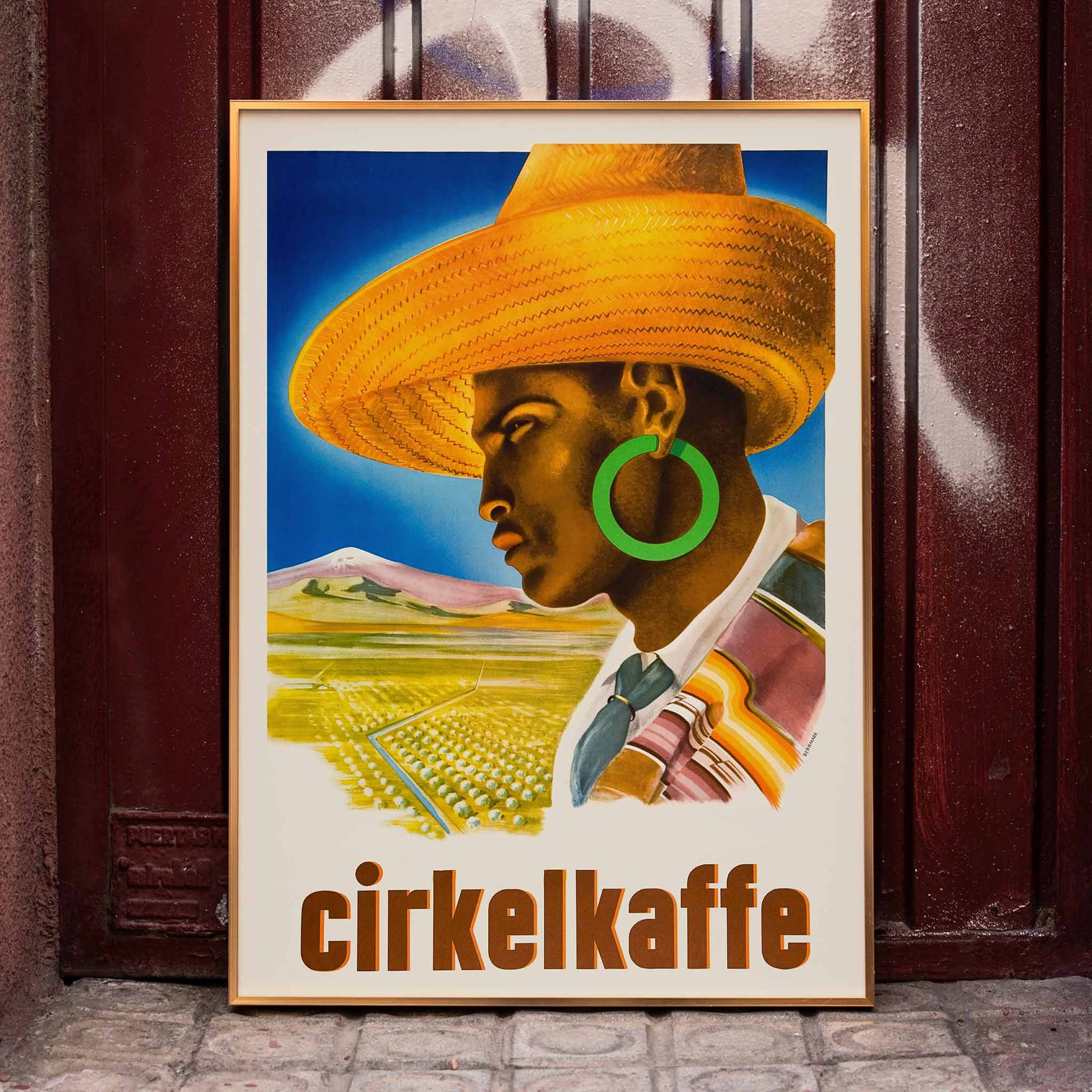 Cirkelkaffe by J Olsens poster featuring a person in a large hat with green earrings and a scenic landscape agricultural background, framed and displayed in home decor