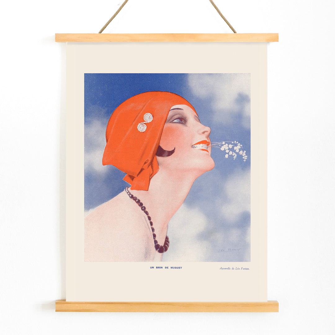 Poster of Un Brin de Muguet by Leo Fontan showing a smiling woman in a red headscarf holding lily of the valley in her mouth, with wooden magnetic frame on white background